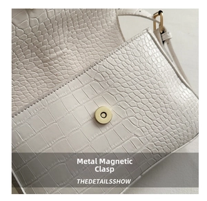 Detail einer weißen Tasche mit Krokodilprägung und goldenem Magnetverschluss