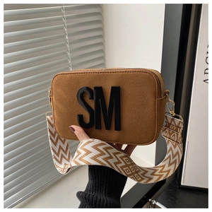 Détail du sac caméra en daim marron avec logo SM et large bandoulière ethnique