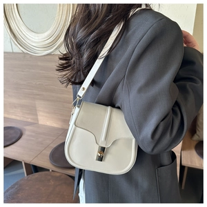 Close-up of beige leather saddle bag featuring a polished metal twist lock closure