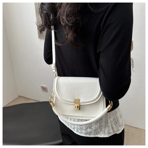 Modern white faux leather saddle bag with gold buckle shown on a model's shoulder