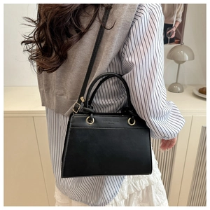 Detailed view of black matte leather handbag with gold lettering and adjustable shoulder strap
