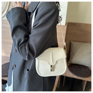 Detail shot of a minimalist cream leather saddle bag with silver metal twist lock on gray blazer