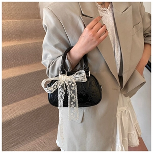 Close-up of black leather mini handbag featuring white lace bow and embossed patterns