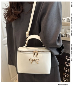 Detail of white structured box bag with gold bow clasp shown on a grey blazer model