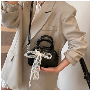 Close-up of black glossy mini bag featuring logo embossing and a white lace bow detail