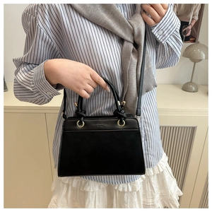 Detail of a black leather handbag featuring gold Fashion Trend text and dual handles