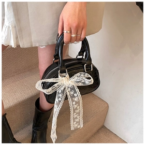 Detail of vintage black glossy handbag with white lace bow and embossed patterns