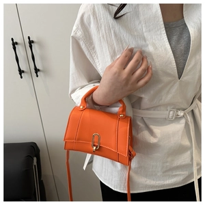 Détail d'un sac bandoulière orange vif avec un fermoir pivotant ovale en métal doré