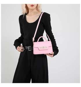 Close-up of pink leather crossbody bag with gold buckle on a model in a studio set