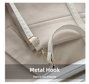 Detail of the golden metal hook and leather strap on a beige canvas box bag