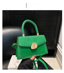 Detail view of shiny green crocodile pattern handbag with golden metal lock and strap