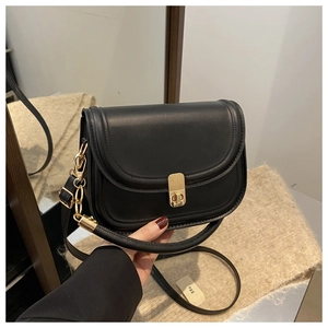 Detail of black saddle bag with golden buckle and chain strap shown in mirror reflection