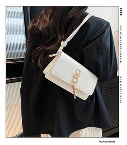 Detail of white crocodile embossed crossbody bag with gold metal tassel buckle and slim strap