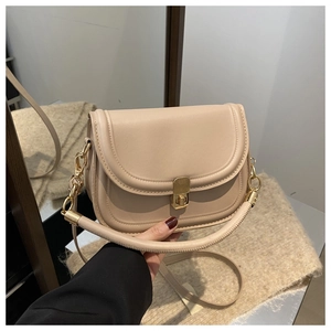 Close-up of beige saddle bag featuring a matte finish and vintage gold metal clasp