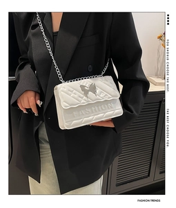 Detail of white quilted handbag featuring silver butterfly buckle and fashion embossed text