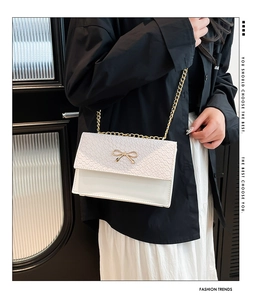 Détail du petit sac blanc en simili cuir avec texture croco et nœud doré élégant