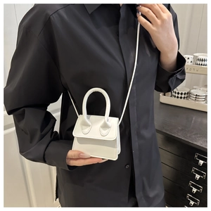 Detailed close-up of a white mini leather crossbody bag shown on a model with black shirt