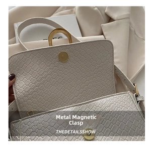 Close-up of the vintage matte gold magnetic buckle on a cream crocodile embossed bag