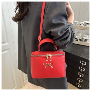 Detail of red leather crossbody bag with golden bow clasp and double zipper closures
