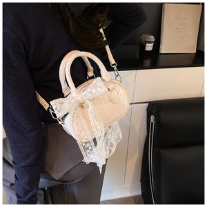 Detail view of cream white PU handbag with embossed texture and lace bow on a model
