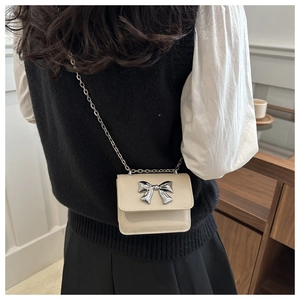 Back view of model wearing a cream mini crossbody bag with silver bow and chain