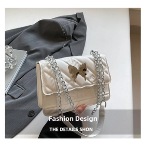 Detail of white quilted crossbody bag featuring a gold butterfly buckle and chain strap