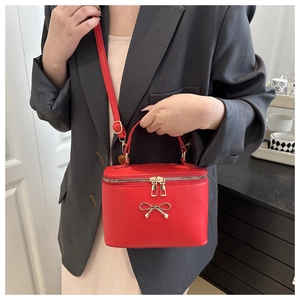 Red box crossbody bag with gold bow detail worn by model in elegant indoor setting