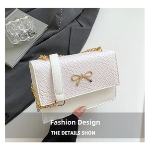 Detailed close-up of white crocodile pattern texture with golden metal bow on small bag