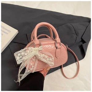 Close-up of pink patent leather handbag with embossed patterns and lace bow detail