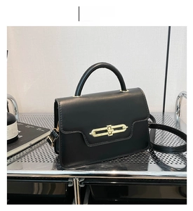 Detail of black crossbody bag with gold chain lock on a metallic mesh display stand