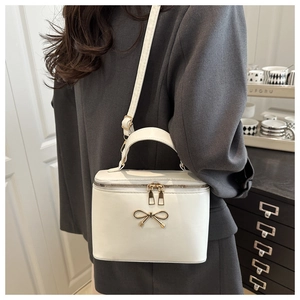 Detail of white box handbag with golden bow buckle and dual zipper on model's shoulder