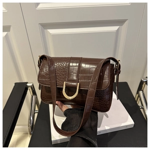Detailansicht der dunkelbraunen Krokodilledertasche mit goldenem D-Verschluss und Textur