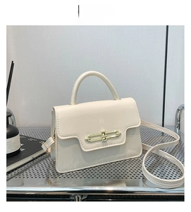 Close-up of off-white crossbody bag with golden rectangular lock on silver grid shelf