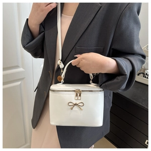 Close-up of a white box bag with a golden metal bow and dual zippers on a model