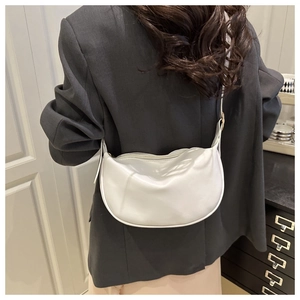White crescent crossbody bag worn over a grey blazer showing soft texture and modern style