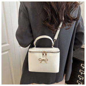 Detailed view of the white square box bag with gold bow and smooth leather texture