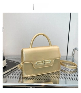Detail view of a gold shiny square handbag with adjustable strap and metal lock