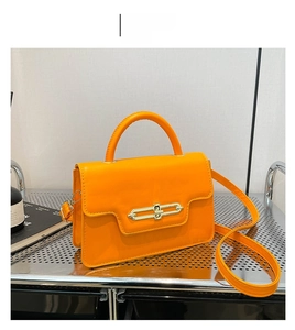 Detailed view of an orange leather crossbody bag with golden metal clasp and top handle