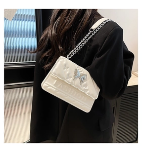Detail of white quilted crossbody bag featuring silver butterfly clasp and fashion embossing