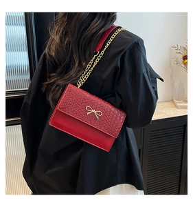 Detail of red crocodile texture handbag with gold bow hardware on a female model