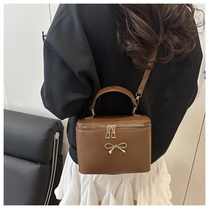 Detail of a dark brown box bag featuring a delicate gold bow and textured PU leather