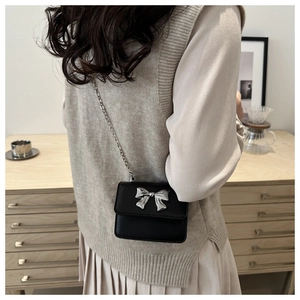 Detailed back view of a mini black crossbody bag with a silver bow and metal chain
