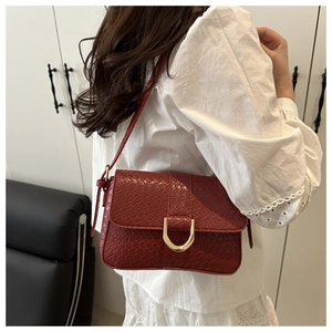 Detail of burgundy crocodile-embossed leather baguette bag with a gold horseshoe buckle