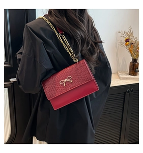 Detail of dark red crossbody bag with snake pattern flap and golden bow clasp