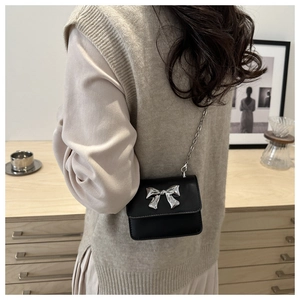 Detail of mini black crossbody bag with silver bow accent and delicate chain strap