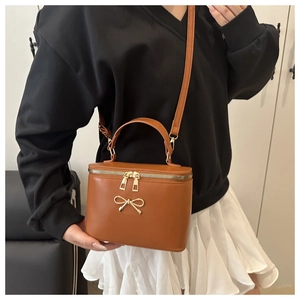 Detail of caramel leather box bag with gold bow ornament and dual metal zippers