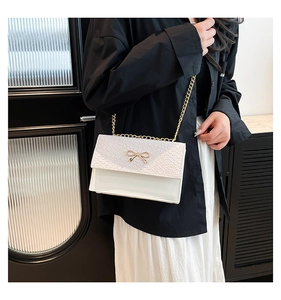 Détail du sac blanc à chaîne avec rabat texturé et nœud papillon doré décoratif