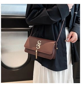Detail of brown faux leather shoulder bag with crocodile texture and gold S-buckle tassel