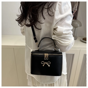 Detail of a black box bag featuring a gold bow accent and metallic zippers for women