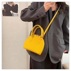 Vibrant yellow faux leather handbag with crocodile pattern worn by a model in gray blazer